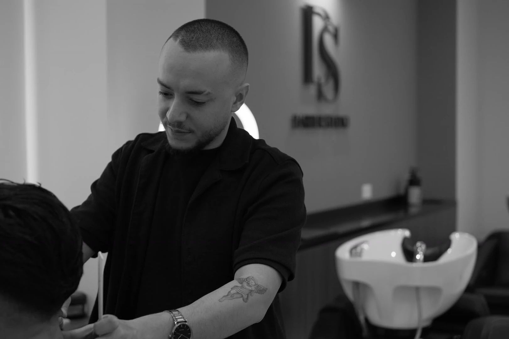 A barber at the wash basin, the DS monogram on the wall behind him.