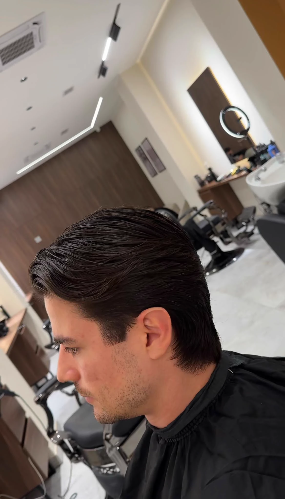 A client in profile with a finished swept-back cut, the studio behind him.