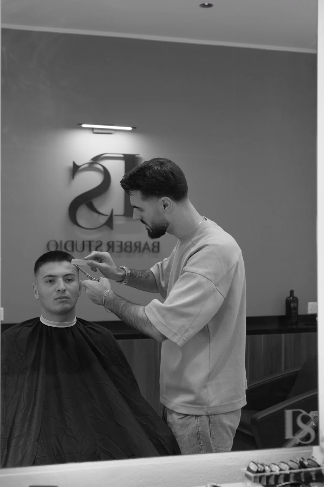 A barber cutting in front of the mirror, the DS monogram on the wall.