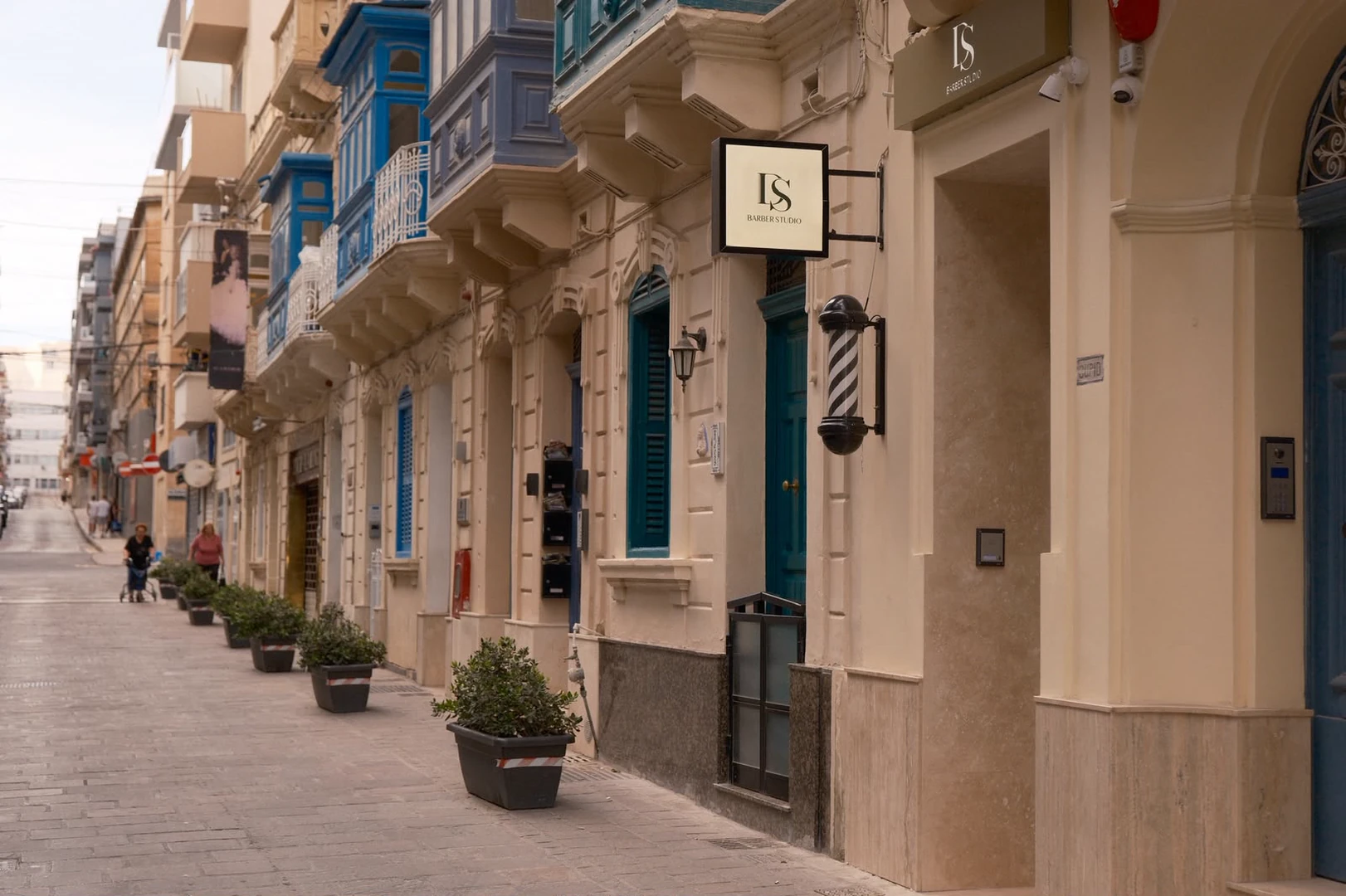 Triq Manoel De Vilhena in Gżira: limestone façades, teal timber balconies, and the DS Barber Studio sign and barber pole.